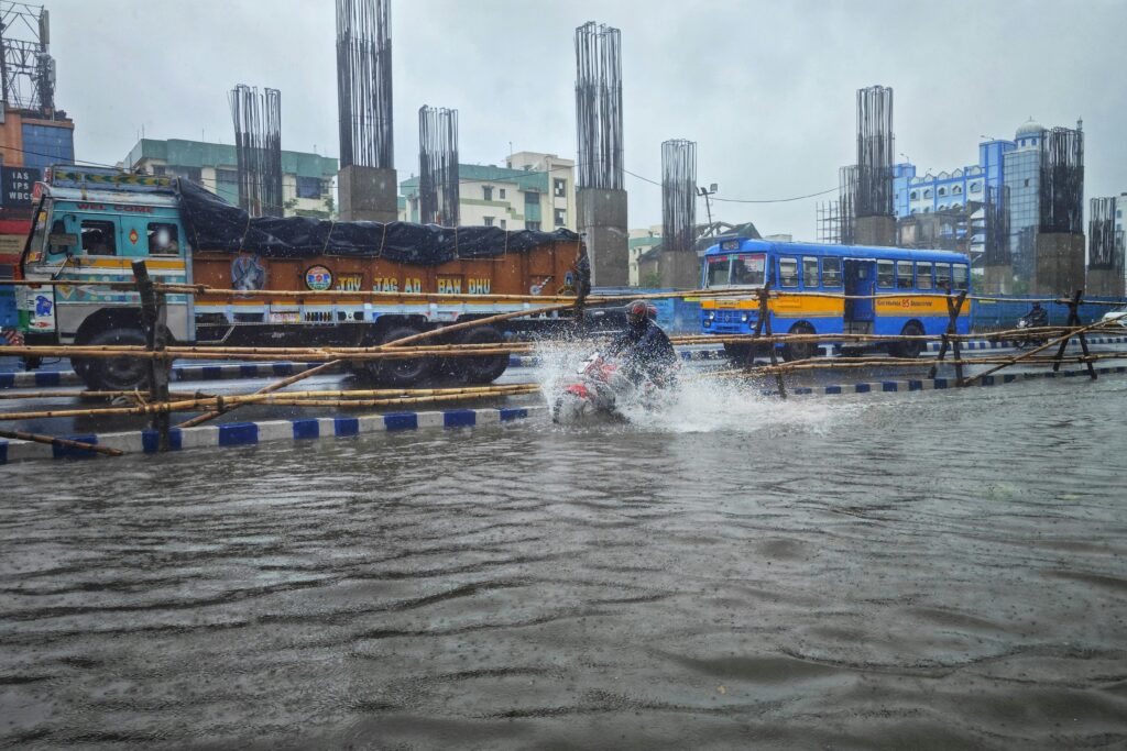 A motorbike navigates a flooded street in Kolkata, India, amidst urban traffic.