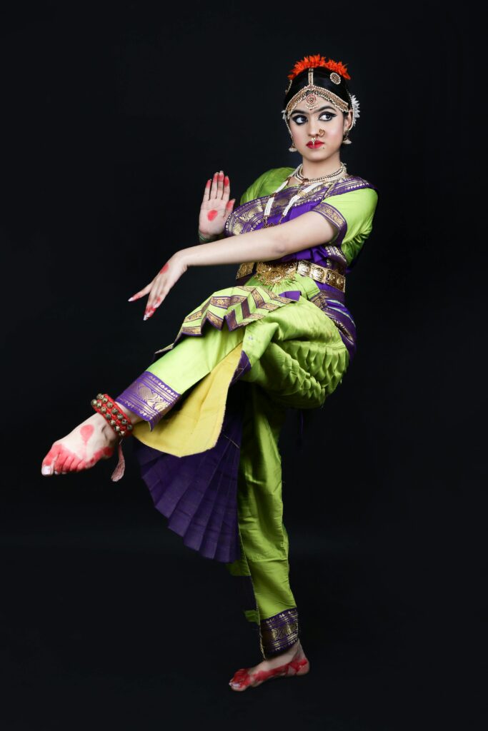 Graceful Indian dancer posing in vibrant traditional clothing with intricate jewelry on a black background.